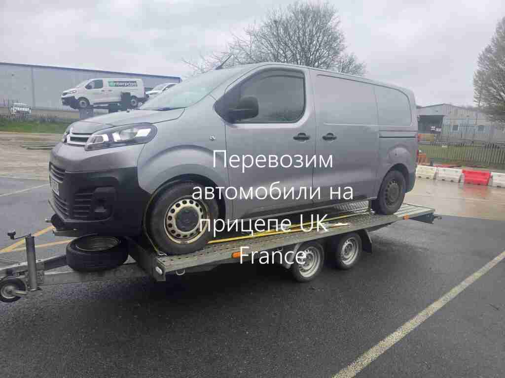 На фото показан серый фургон, закреплённый на двухосном автомобильном прицепе. Машина надёжно зафиксирована ремнями, что подчёркивает возможность безопасной Перевозим автомобили на прицепе UK – France