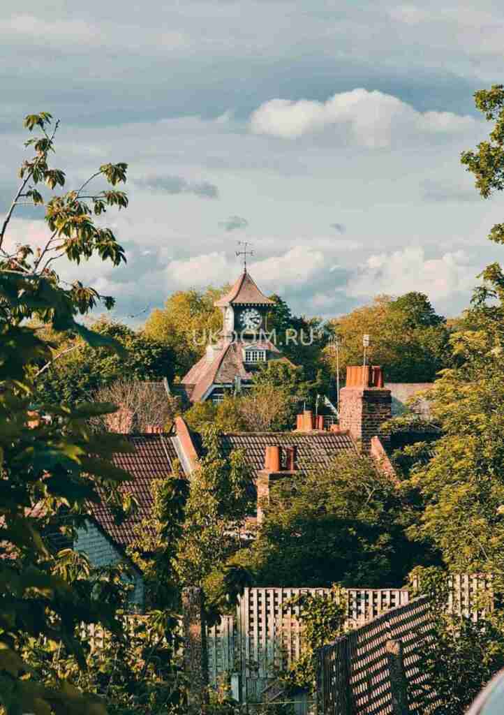 Scenic view of a quaint English village featuring a historic clock tower surrounded by lush greenery.