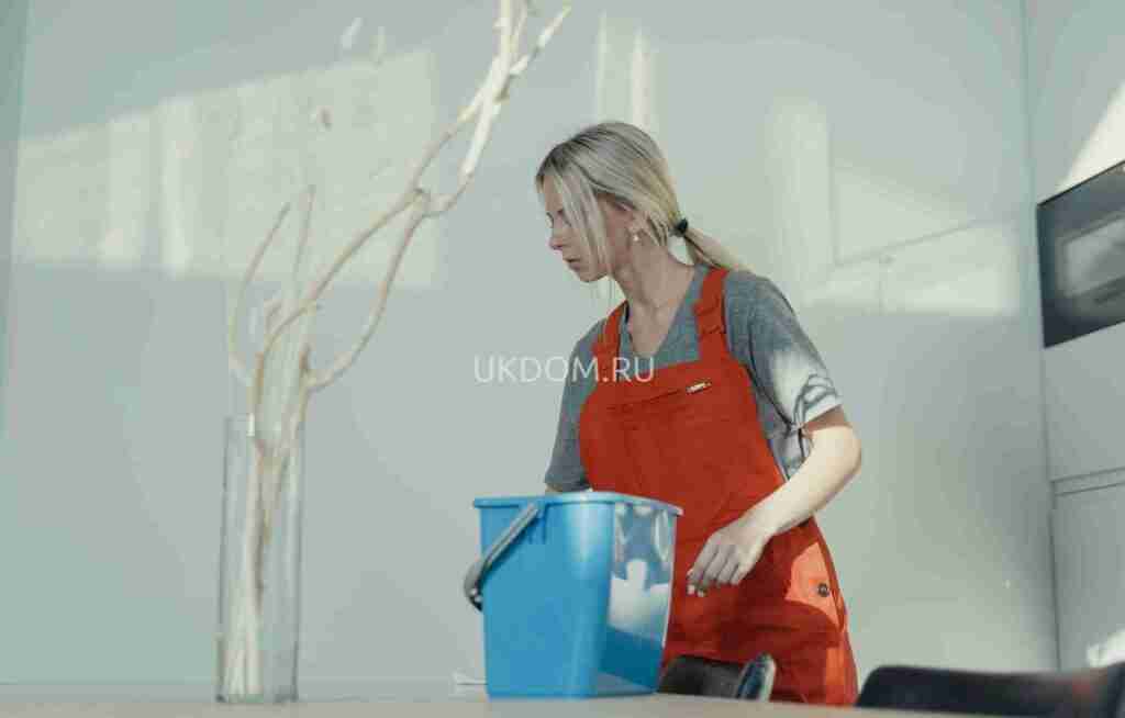 A woman in a red uniform cleans indoors with a blue bucket, ensuring a spotless environment.