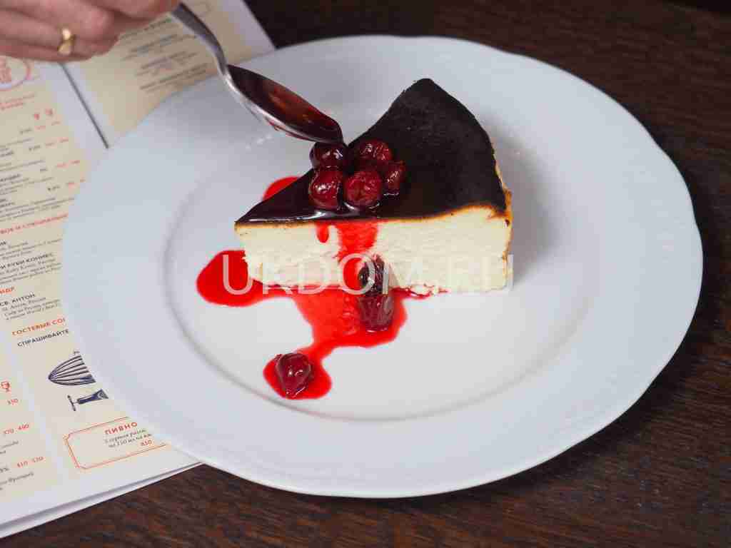 Close-up of a cheesecake slice with cherry sauce on a white plate, perfect dessert choice.